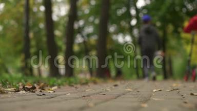 两个青少年手里拿着一辆滑板车和一块便士板跑步。 他们沿着公园的小路前进。 仍在关注